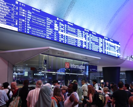 A crowd of people in front of an information screen at a station