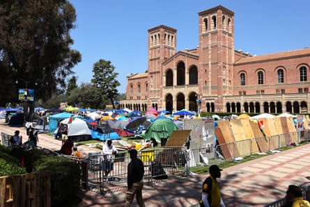 A number of tents set up in the foreground with a brick building standing tall in at the back.