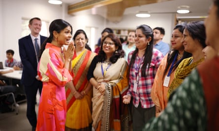 Akshata Murty stands talking to a group of six women in a meeting room while a man ina a suit looks on smiling