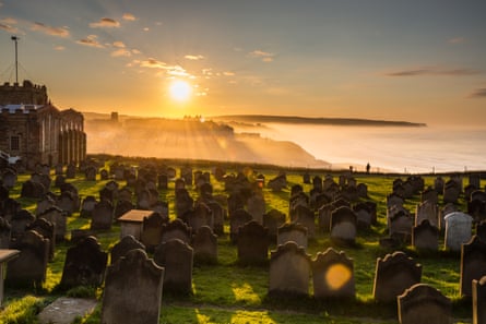 sunlight shining on the graveyard at St Mary’s in Whitby with a view of the sea and beach