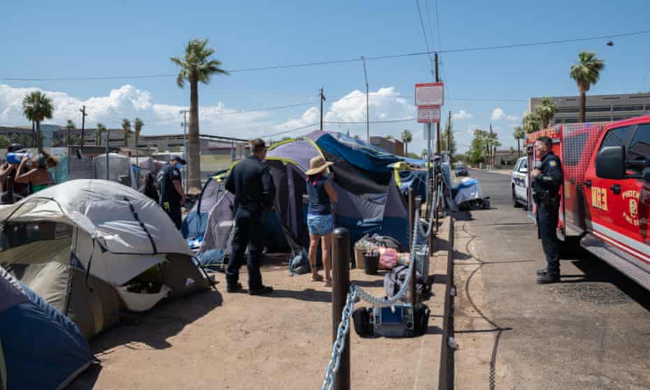 Stacey Champion talks with the Phoenix Fire Department after meeting someone who seemed to be suffering from heat stroke while passing out water and cooling towels to unsheltered neighbors staying in The Zone on June 11, 2022, in Phoenix, Ariz.