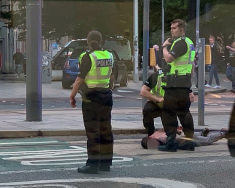 Two police officers in high-visibility vests stand over a person lying on the ground on a street