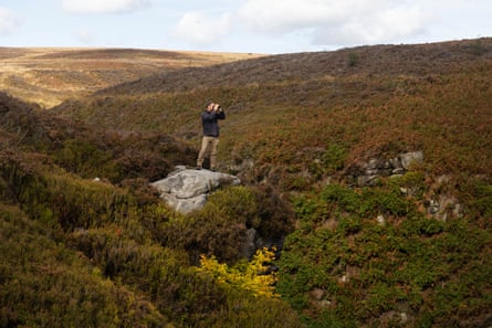 Mark Cocker standing on a rock looking through binoculars.