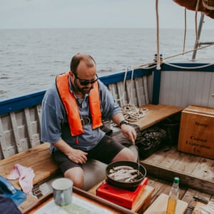 Chef Charlie Hodson prepares cooked breakfast on board the Salford whelk boat, Norfolk, UK.