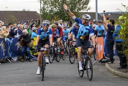 Sir Chris Hoy and wife Sarra wave to onlookers as they ride bikes down a road.