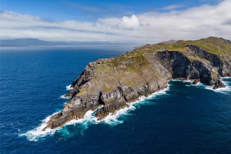 A spectacular rocky peninsula with steep cliffs and green grassland jutting into deep blue ocean water with white surf