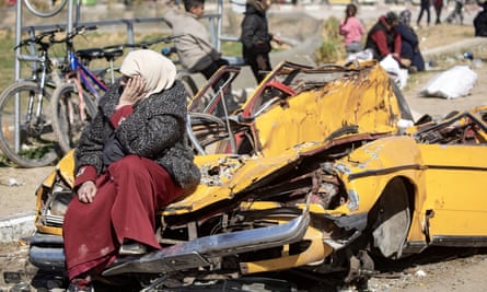 A displaced Palestinian woman rests on a destroyed vehicle after the Israeli army told residents of the Khan Younis refugee camp to leave their homes
