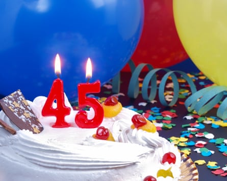 A birthday cake with ‘45’ in candles on it and balloons and party strings.