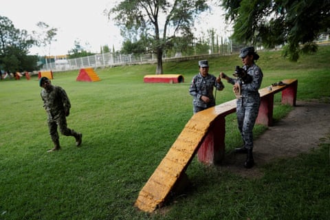 Two women in fatigues with chihuahua in grassy field with painted cement stairs and balance areas.