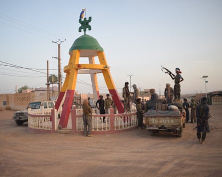 Armed men gather at a structure in the green, red and yellow colours of Mali's flag