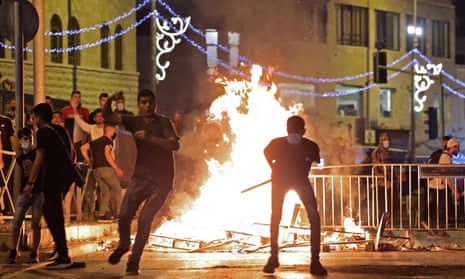 silhouettes of people against a blazing fire and metal barricades, at night