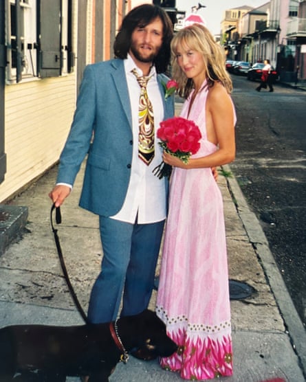 She wears a patterned, pink-looking dress and stands next to her spouse in a blue suit.