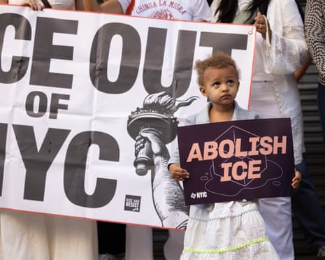 A little girl, maybe three or four, looks up as she holds a sign that says "Abolish ICE" in front of adults holding a banner that appears to say "ICE out of NYC."