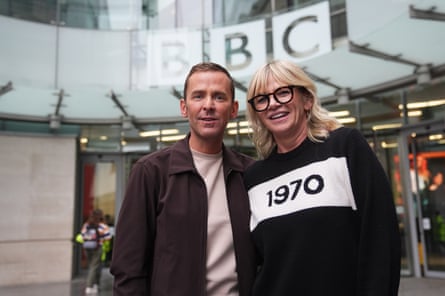 Zoe Ball and Scott Mills outside Broadcasting House with a BBC logo behind them in the glass above the entrance.