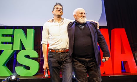 Bas Eickhout and Frans Timmermans hold microphones with their arms around each other's shoulders on a stage