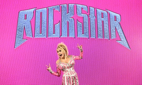 دالي پارتون با لباس ستارهاي صورتي دراماتيك در حال ژست گرفتن در مقابل پس زمينه صورتي با عنوان آلبوم Rockstar با حروف بزرگ