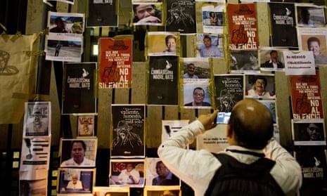 A man takes a picture of images of murdered journalists taped to a fence outside the interior ministry building in Mexico City.