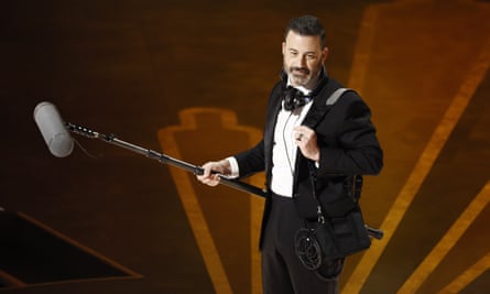Jimmy Kimmel dressed in black tie while holding a boom mic, hosting the Oscars