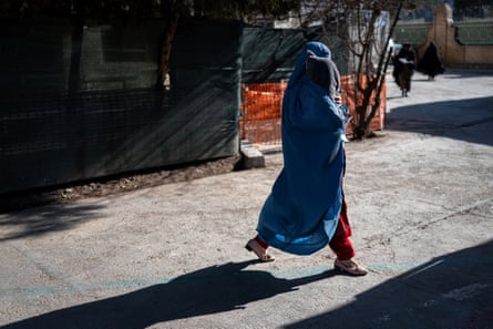 A woman wearing a blue burqa walks with a small child in her arms