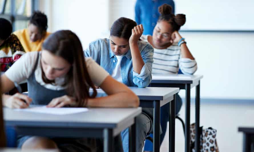 Young multi-ethnic female university students writing on papers at desks during exams in community college classroom