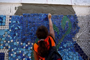Guatire, Venezuela. A woman sticks plastic bottle tops on to cement in a section of a 270 sq-metre mural by Venezuelan artist Oscar Olivares