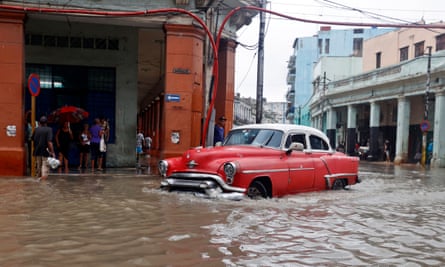 A red vintage car travels through a flooded street in Havana, Cuba, while people shelter in doorways