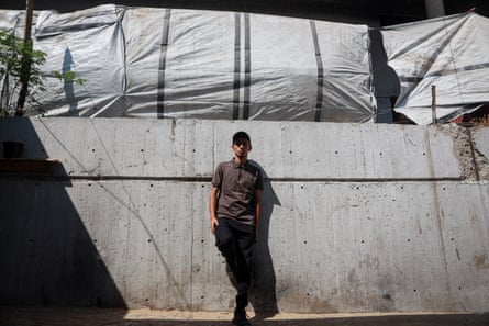 A man stands against a concrete wall with tarpaulins rigged above it