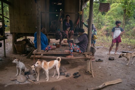 A group of people sit on a wooden platform outside a hut on stilts.