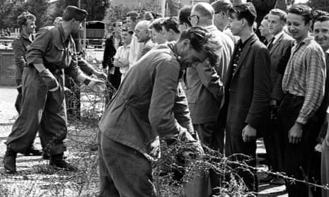 East German soldiers set up barbed wire barricades to restrict travel between the eastern and western part of Berlin. West Berlin citizens watch the work, 13 August 1961.