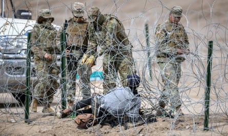 four people in military clothing untangle barbed wire with another person lying on the ground