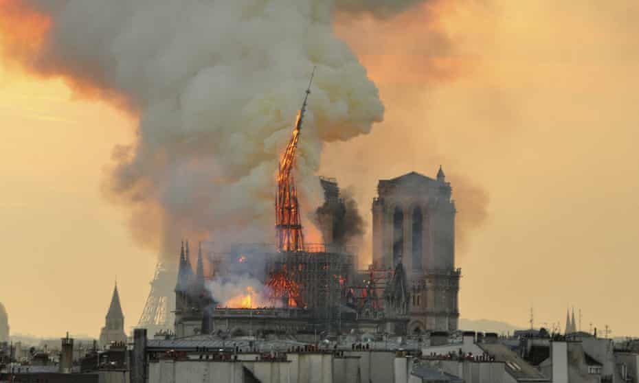 The flaming spire of Notre Dame Cathedral topples into the roof. 