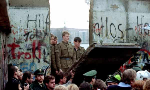 East German border guards look through a hole in the Berlin Wall in November 1989
