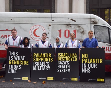 Five protesters holding placards stand in front of a van made to look like a damaged Gaza ambulance