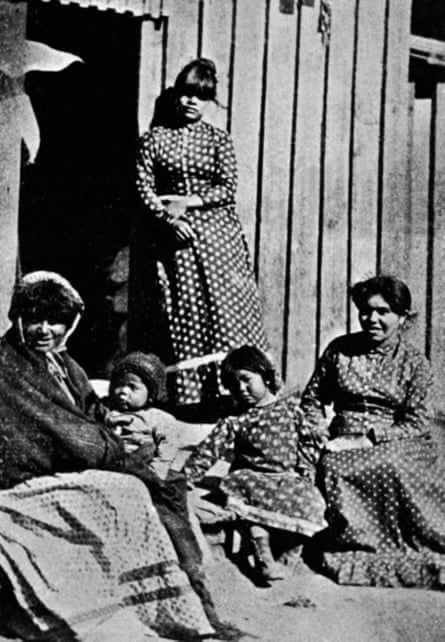 A black and white photo of women and children in western-style gowns in front of a wood-clad building.