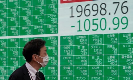 A man in a mask walks past a screen displaying information from the Tokyo stock market