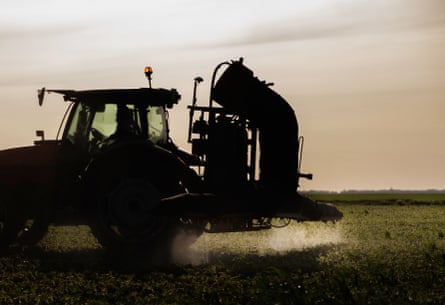 A tractor sprays pesticide over a green field.