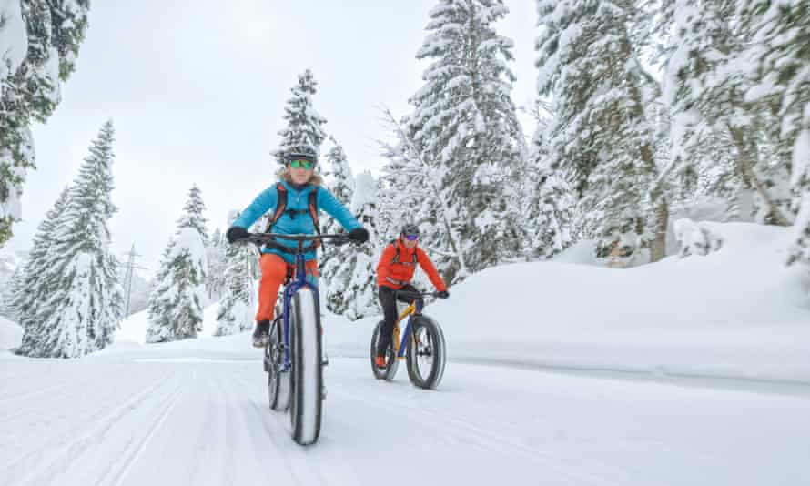 Male and female mountain bikers riding fatbikes on snow covered landscape.