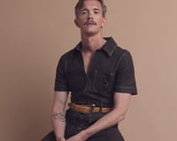 Stephen Libby sits on a wooden stool, wearing a dark denim jumpsuit and boots