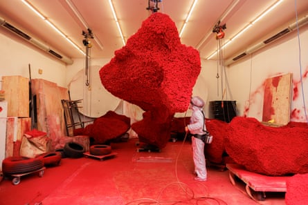 A person in a hazmat suit working on a big, red sculpture.