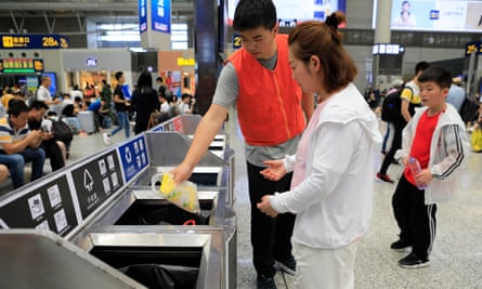 A volunteer helps a woman sort garbage in front of recycling and rubbish bins at Hongqiao railway station in Shanghai.