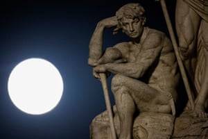The full moon rises behind a statue in Rome, Italy
