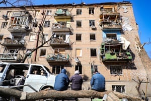 People sit on a log in front of an apartment building damaged as a result of shelling by the Russian troops in Podilskyi district of Kyiv.