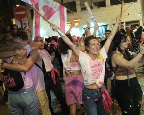 Oamenii se îmbrățișează și flutură steaguri printre confetti care cad în timp ce sărbătoresc ieșirea din urne la Tel Aviv.