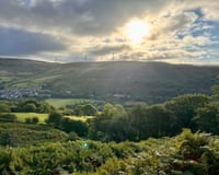 A view across a valley towards sunlit hills with wind turbines and a village off to the left