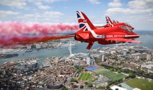 Two Red Arrows perform a flypast over Portsmouth with red and blue smoke emerging from behind