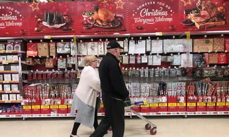 A woman pushes a shopping trolley past Christmas decorations in a Tesco store in Manchester