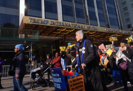 People march with signs past high-rise building with gold awning.