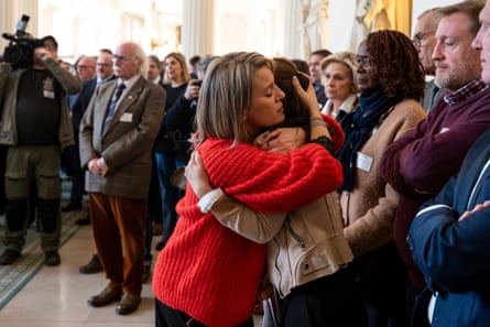 Two women, standing in a crowd of people. hug each other at a memorial event at the Belgian federal parliament