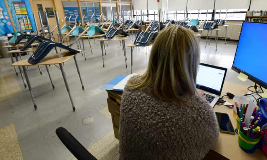 A teacher, her back to the camera, types into her laptop in an empty classroom in Racine, Wisconsin.