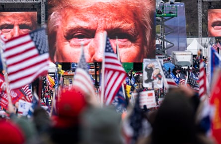 Trumps face shown on screens as a crowd of people wave American flags
